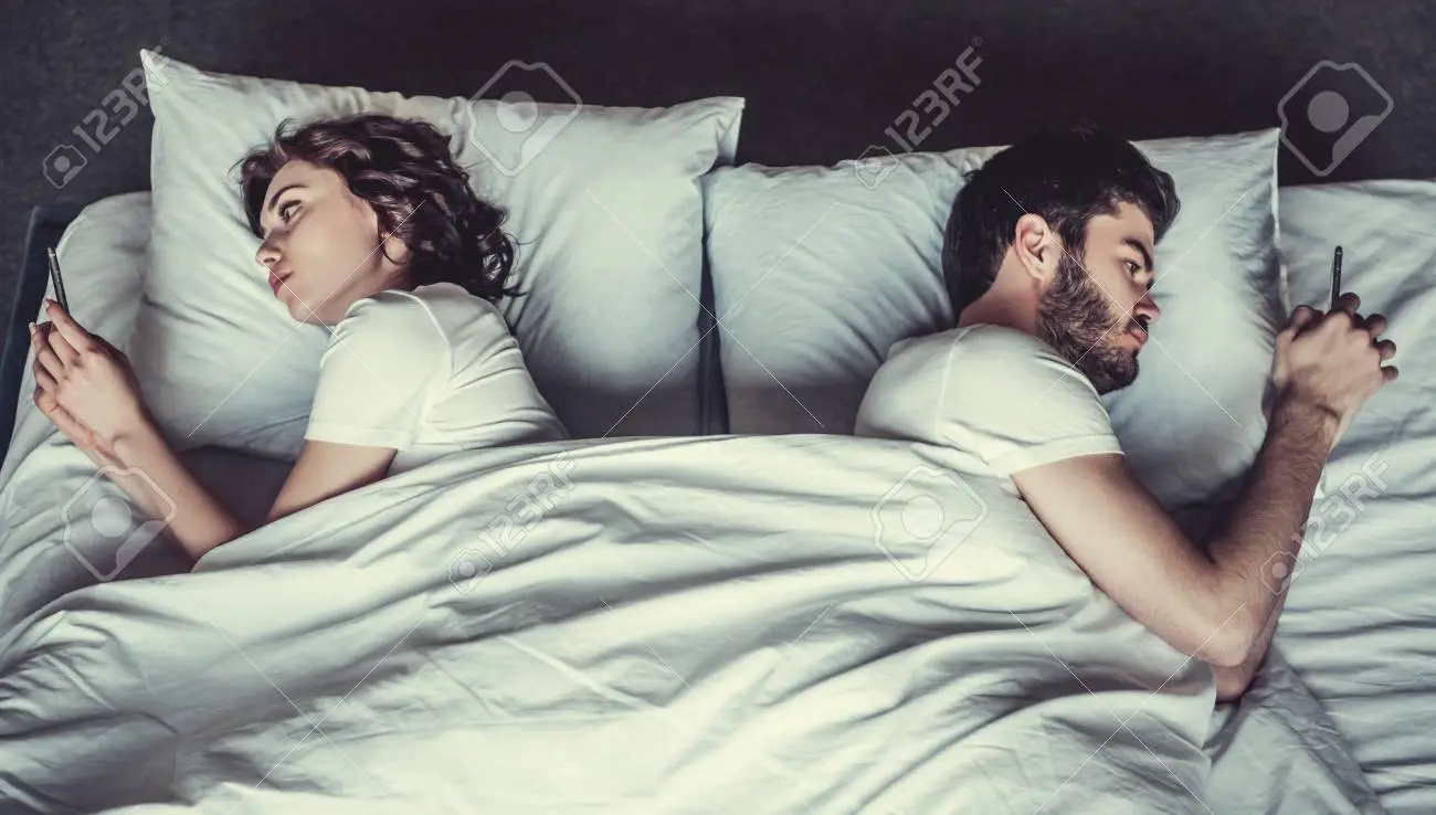 young-couple-in-bed-using-phone-lying-backs-to-each-other